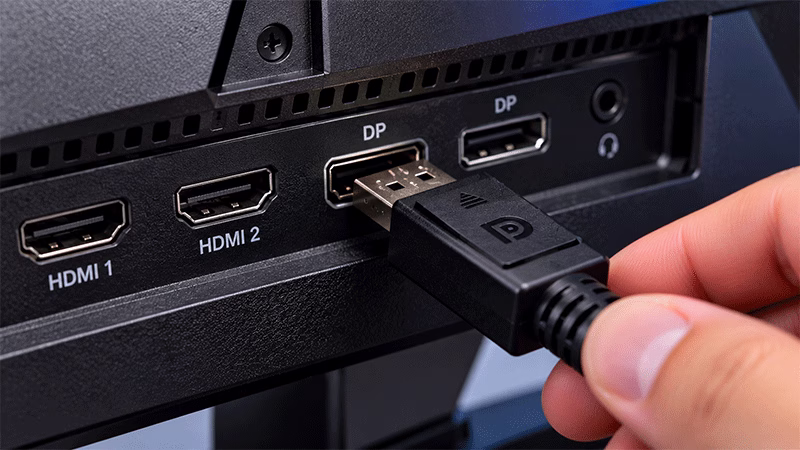 Detalhe de um cabo DisplayPort sendo conectado na entrada traseira de um monitor gamer para alcançar a frequência máxima.